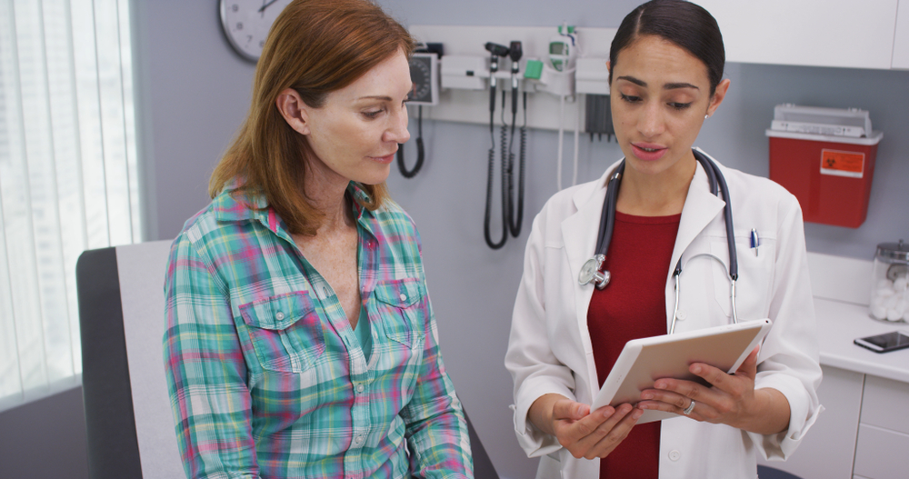 A nurse practitioner shows a patient a tablet in a hospital room.